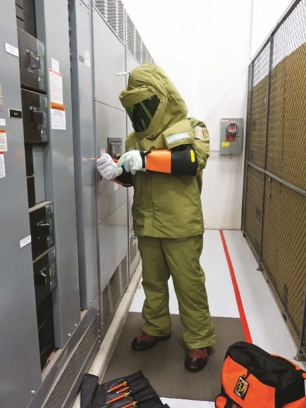 Technician in arc-flash protective suit performing MV switchgear testing